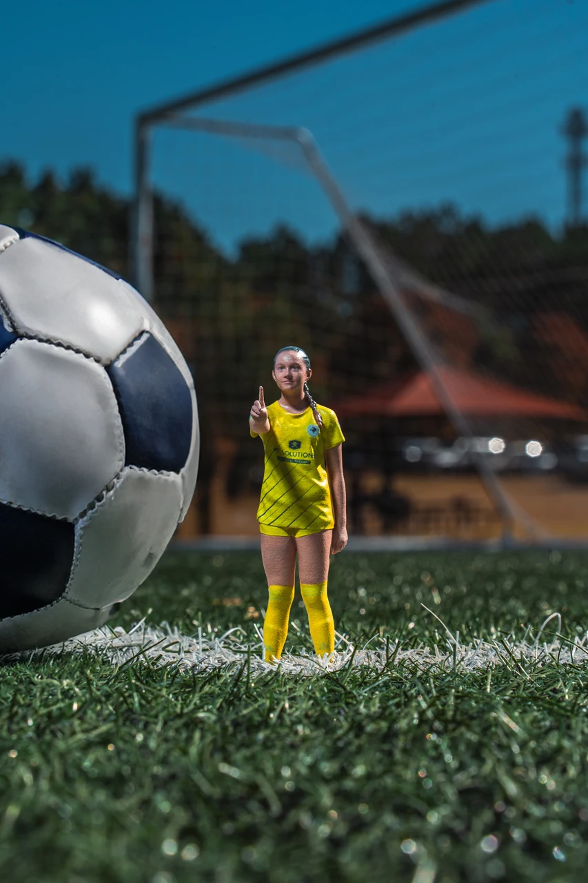 Miniature 3D-printed replica of a young soccer player standing next to a full-size soccer ball for scale